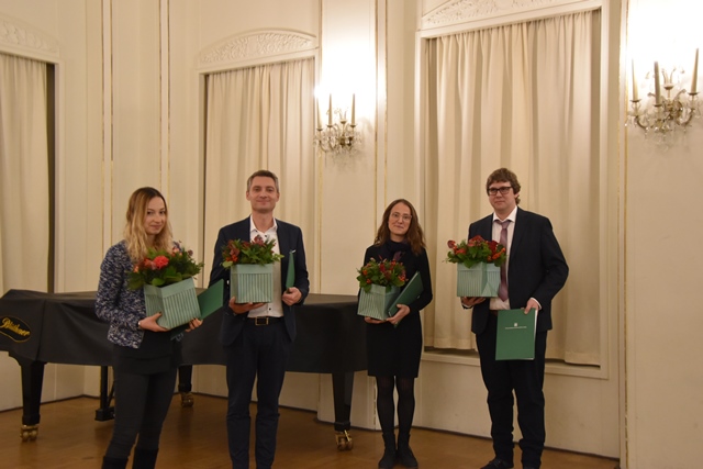 Zwei männliche und zwei weibliche Personen stehen vor einem Flügel und halten Blumensträuße in den Händen.