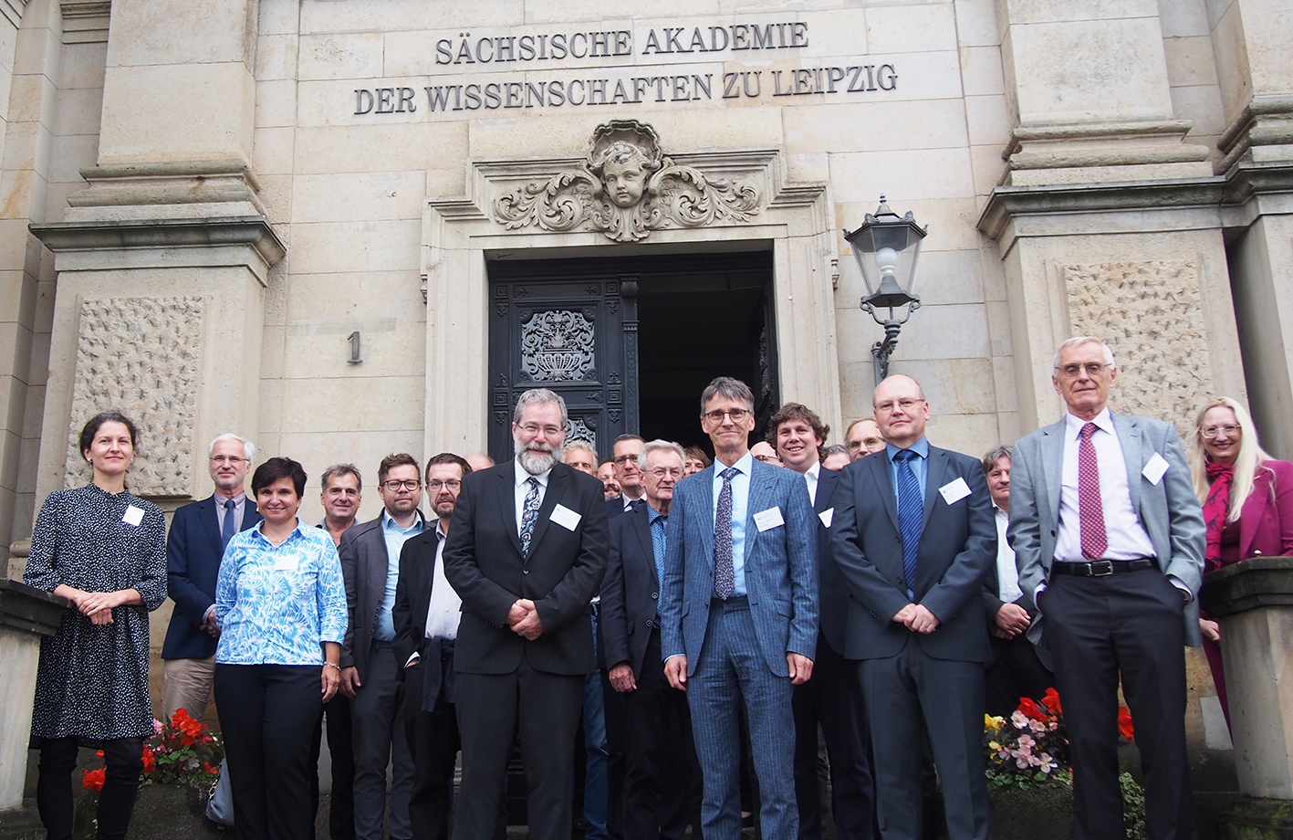 Eine Gruppe von Menschen steht  vor einem Gebäude. Über der Tür liest man den Schriftzug Sächsische Akademie der Wissenschaften zu Leipzig.