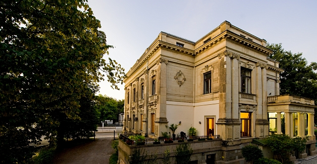 Rückseite einer historischen Villa, links im Bild steht ein Baum