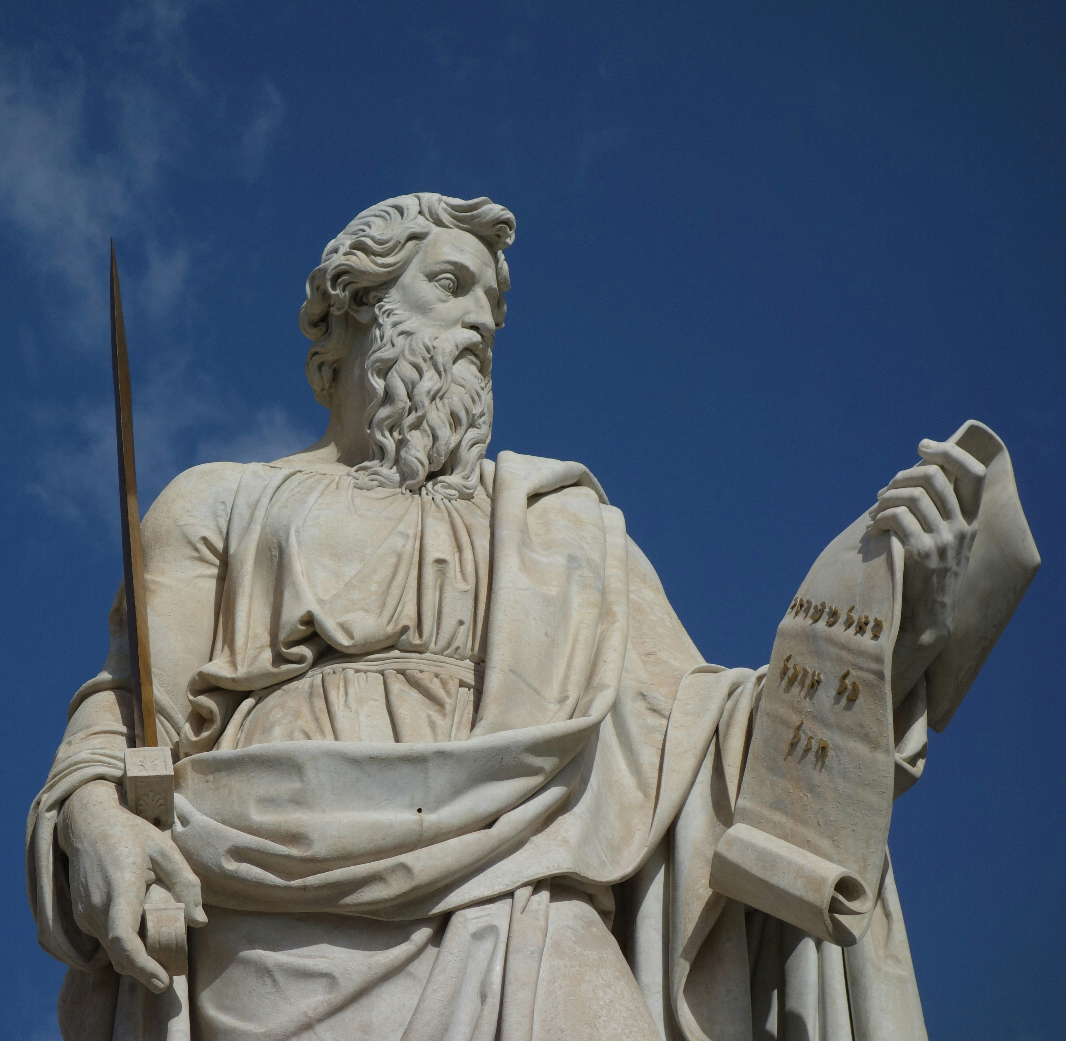 Marmorstatue eines bärtigen Mannes vor blauem Himmel. In der rechten Hand hält er ein Schwert, in der linken eine Schriftrolle mit hebräischen Buchstaben.