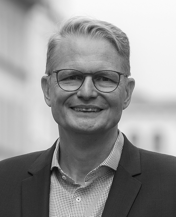 Schwar-weiß-Porträtfoto einer lächelnden männlichen Person mit Brille.