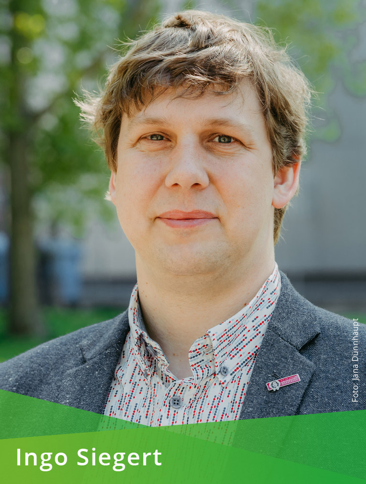 Farbporträt einer männlichen Person im Freien vor einem Gebäude und einem Baum. Auf dem unteren Bildrand steht auf grünem Hintergrund: Ingo Siegert. Im Bild steht außerdem: Foto: Jana Dünnhaupt.