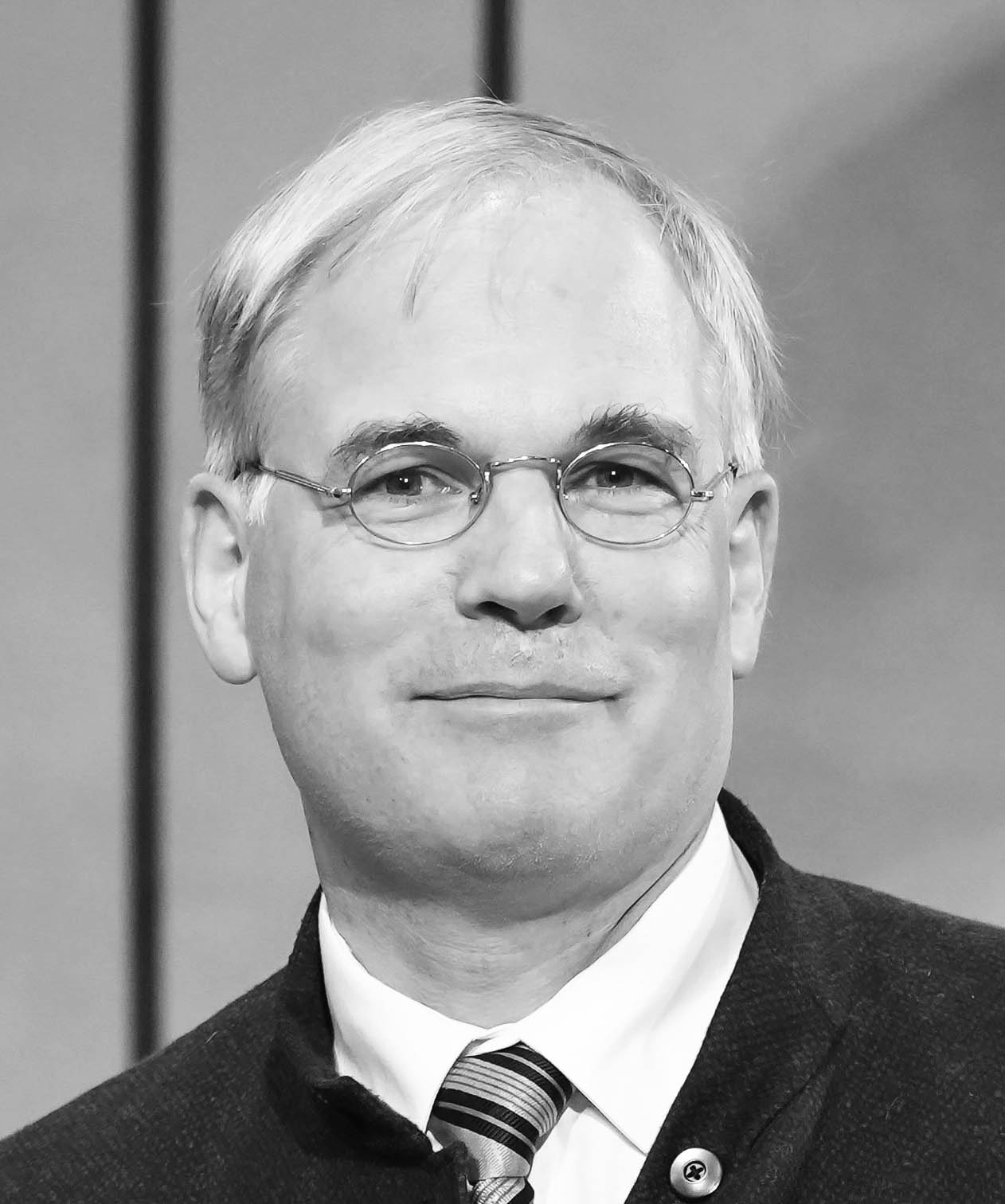 Schwarz-weiß-Porträtfoto einer lächelnden männlichen Person mit Brille und Anzug