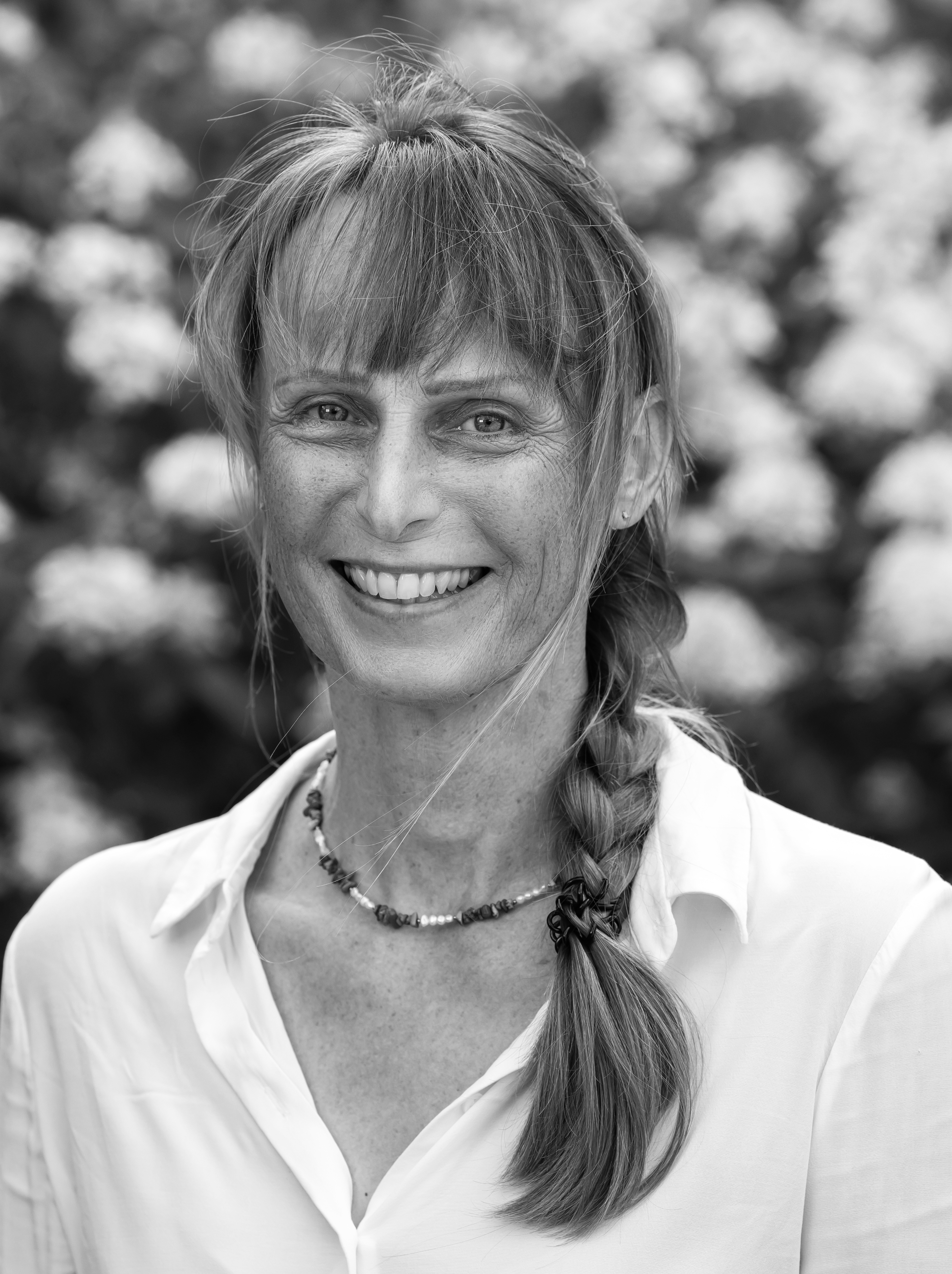 Porträtfoto in schwarz-weiß einer lächelnden weiblichen Person mit weißer Bluse und Halskette in der Natur